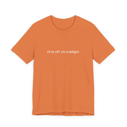 Close-up of folded orange t-shirt showcasing "first off, i'm a delight" printed in white