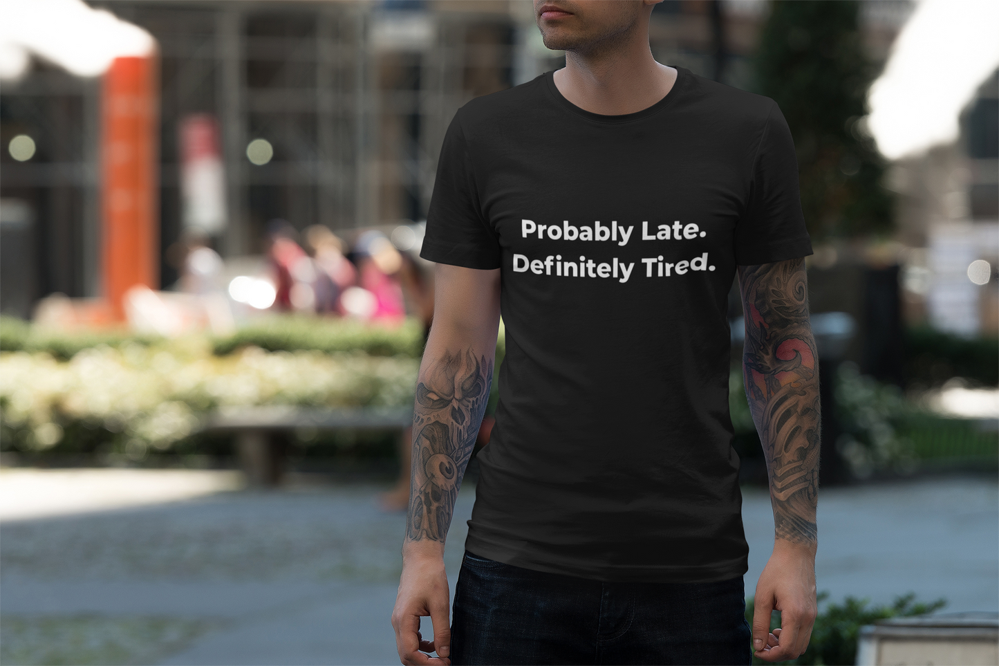 Close-up of a folded black t-shirt with the phrase "Probably Late. Definitely Tired." on a light background.