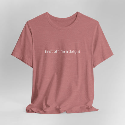 Front view of soft pink t-shirt displaying "first off, i'm a delight" in bold white letters