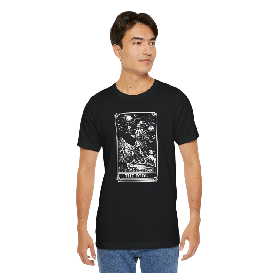 DailyThreadCo. black 100% cotton t-shirt with 'The Fool' tarot card graphic print on the front. Features a skeleton figure, dog, and mountain landscape.