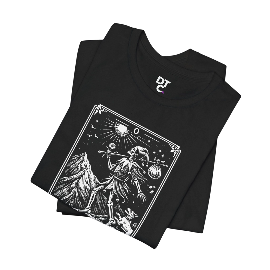 DailyThreadCo. black 100% cotton t-shirt with 'The Fool' tarot card graphic. Features skeleton figure, mountain, sun, and dog.