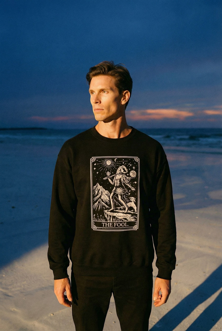 DailyThreadCo. black crewneck sweatshirt with a white graphic of The Fool tarot card, featuring a figure, dog, mountains, and celestial symbols.