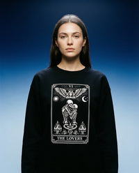 DailyThreadCo. black crewneck sweatshirt with 'The Lovers' tarot card graphic featuring skeleton figures, angelic wings, sun, moon, and flames.