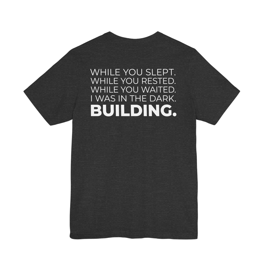 DailyThreadCo. dark grey cotton t-shirt with white text on back: 'While You Slept. While You Rested. While You Waited. I Was In The Dark. BUILDING.'