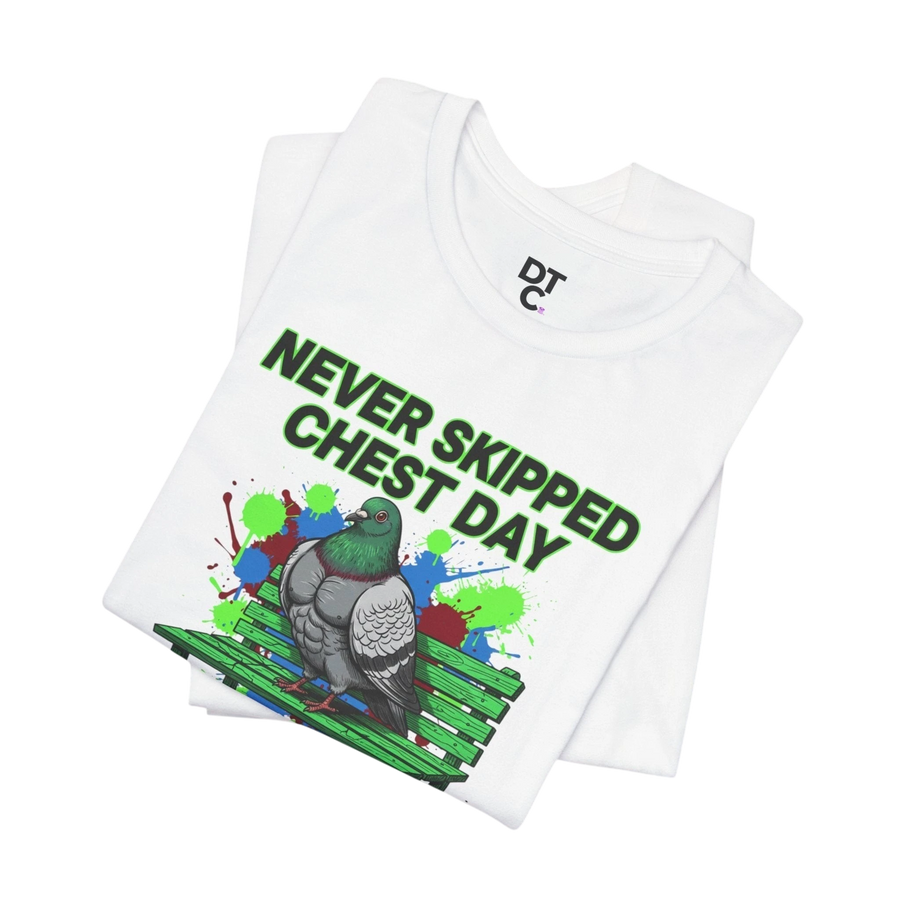 DailyThreadCo. white cotton t-shirt with a graphic print of a muscular pigeon on a green park bench, with colorful paint splatters and text "NEVER SKIPPED CHEST DAY".