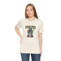 DailyThreadCo. cream 100% cotton t-shirt with a graphic of a raccoon in a trash can with colorful paint splatters and the text 