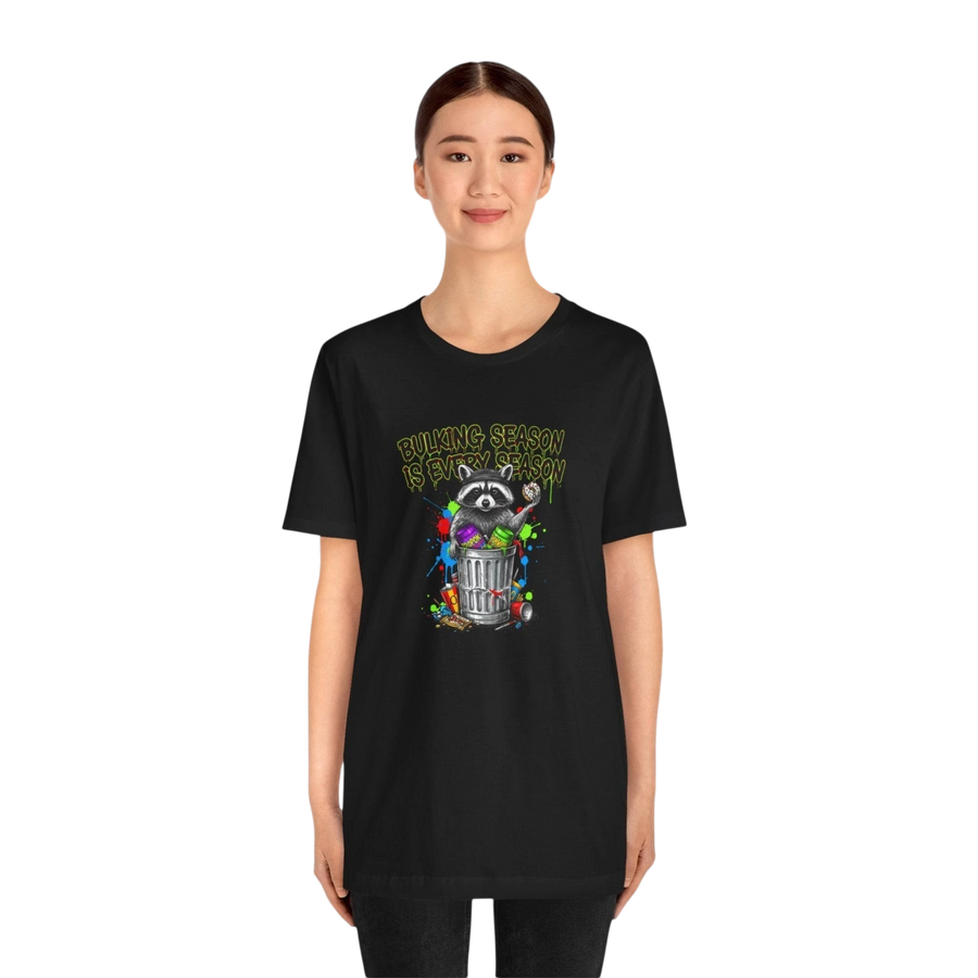 DailyThreadCo. black 100% cotton t-shirt with a funny graphic of a raccoon in a trash can with colorful paint splatters and the text "BULKING SEASON IS EVERY SEASON".