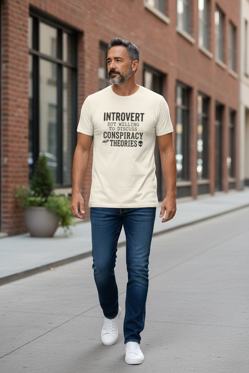 DailyThreadCo. cream cotton t-shirt with black text: "INTROVERT BUT WILLING TO DISCUSS CONSPIRACY THEORIES" and UFO/alien graphics.
