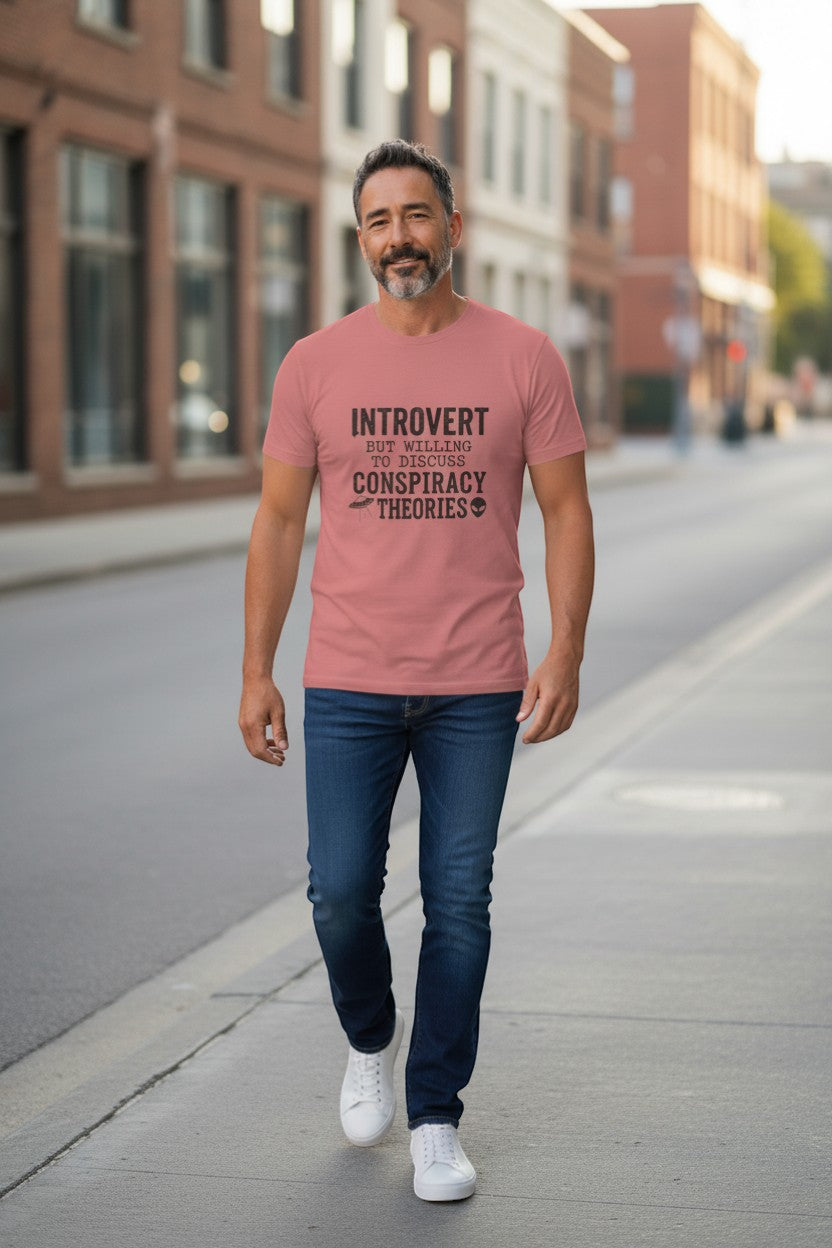 DailyThreadCo. Dusty rose 100% cotton t-shirt with black text: "INTROVERT BUT WILLING TO DISCUSS CONSPIRACY THEORIES" featuring a UFO and alien graphic.