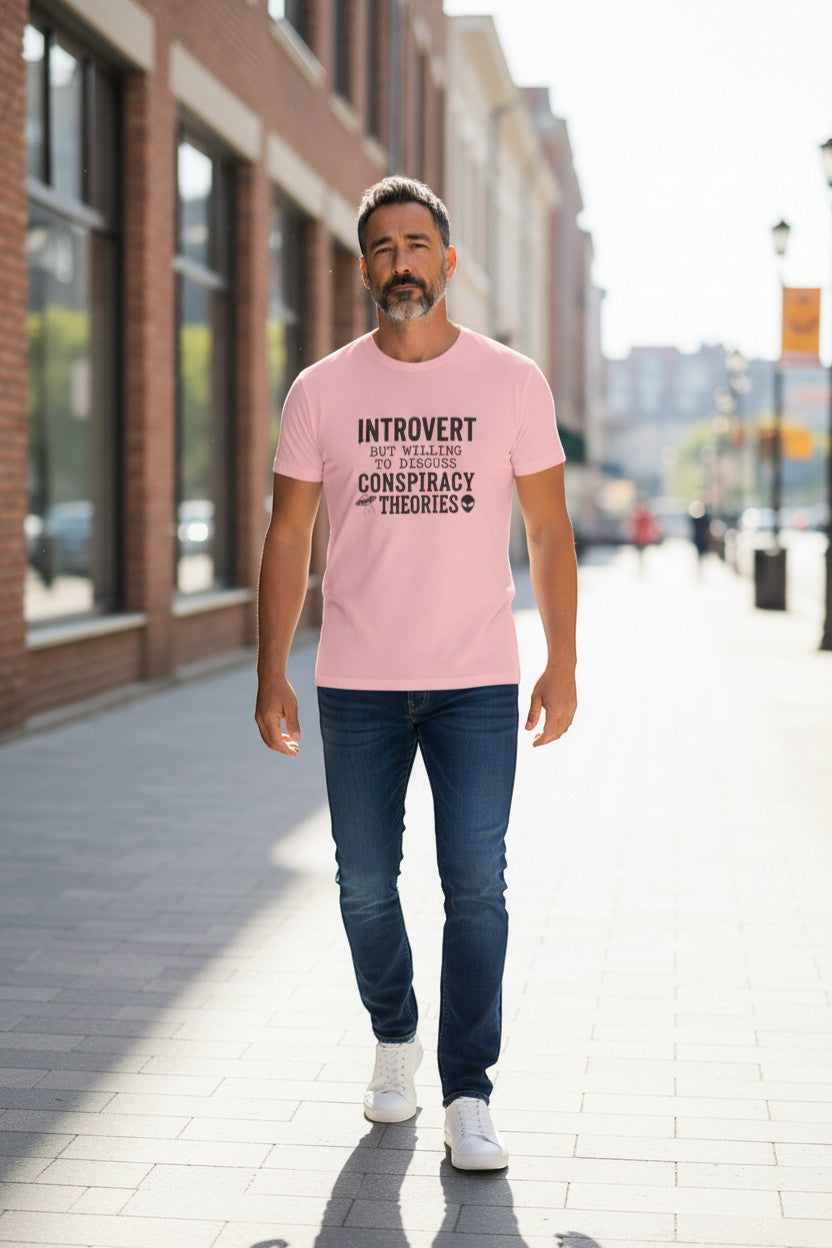 DailyThreadCo. light pink 100% cotton t-shirt with "Introvert But Willing to Discuss Conspiracy Theories" graphic and alien/UFO icons.