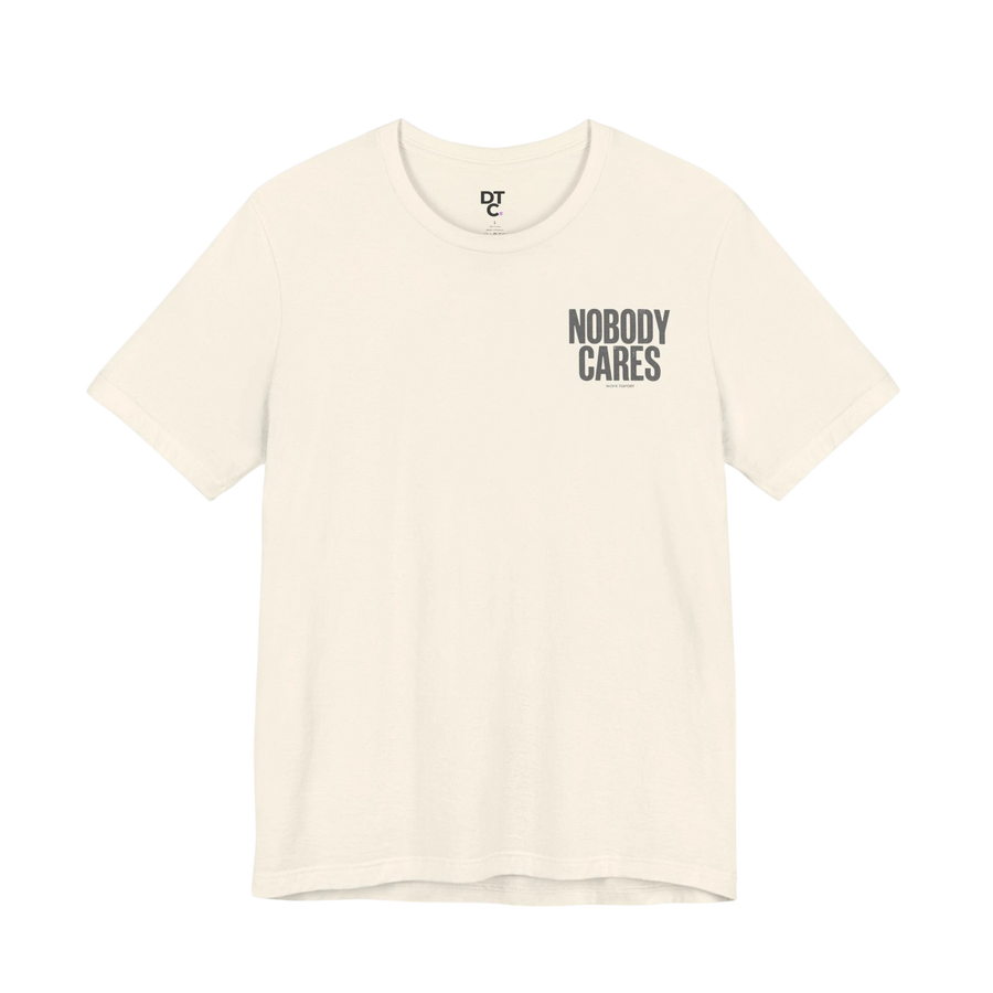DailyThreadCo. cream 100% cotton graphic tee with "Nobody Cares" text art on the chest.