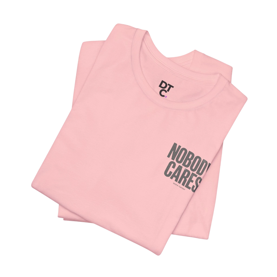 DailyThreadCo. light pink 100% cotton graphic tee with "NOBODY CARES" text art and DTC logo.