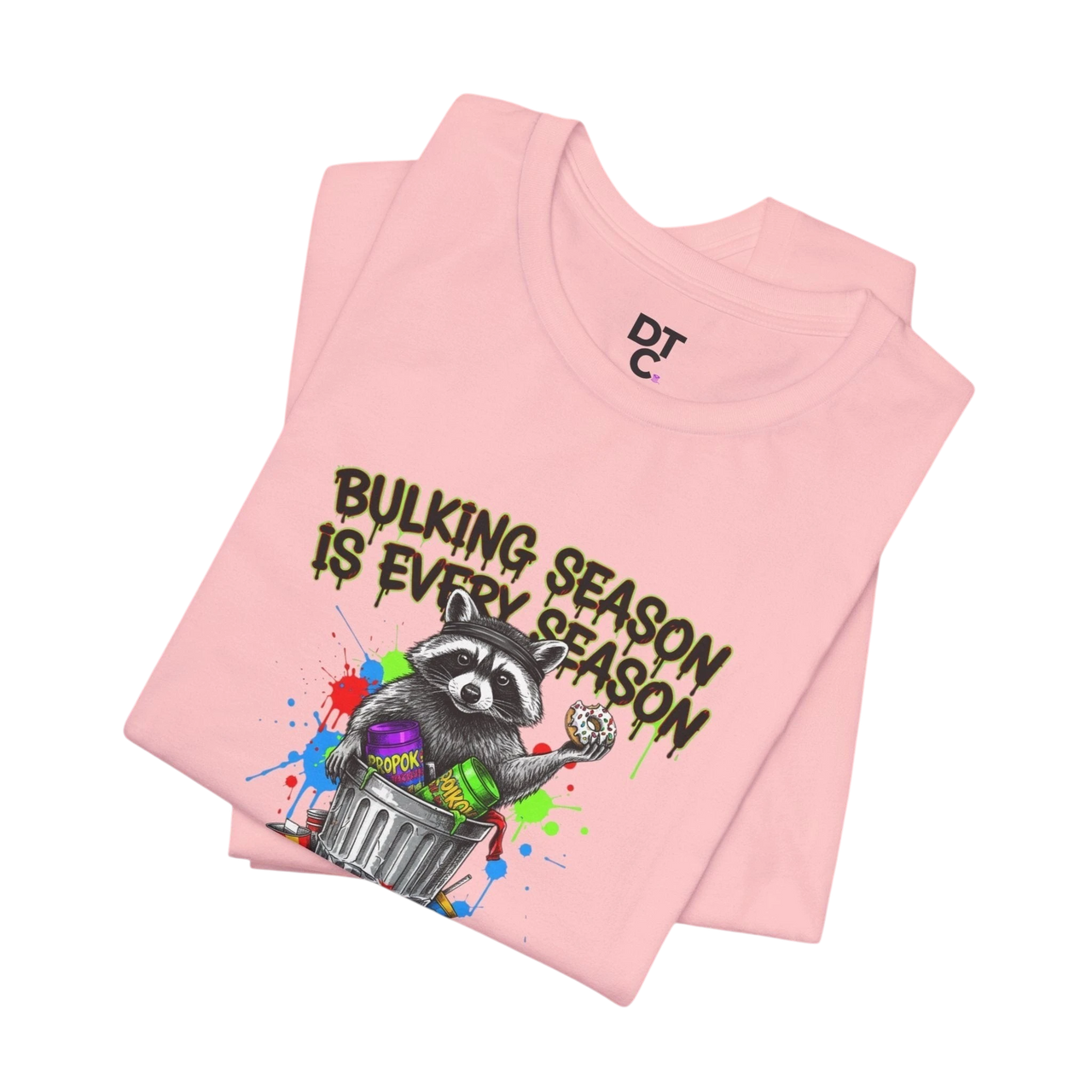 DailyThreadCo. pink 100% cotton t-shirt with a graphic of a raccoon in a trash can holding a donut and the text "BULKING SEASON IS EVERY SEASON".