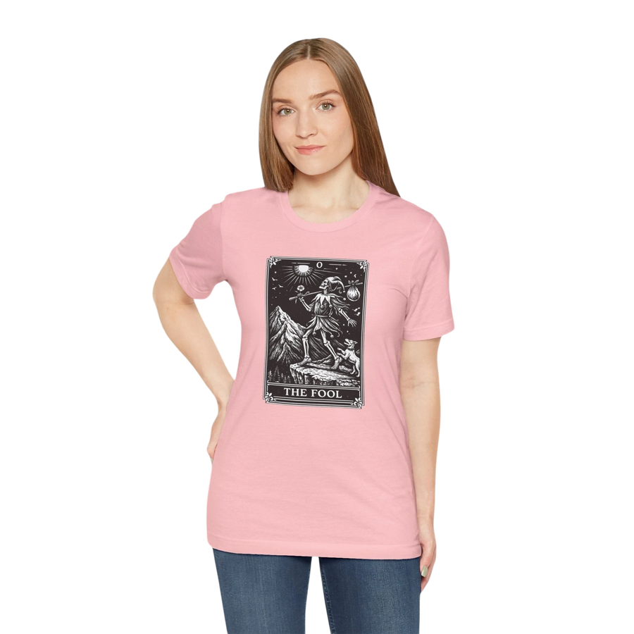 DailyThreadCo. pink cotton t-shirt with a black and white graphic of The Fool tarot card, featuring a skeleton figure on a mountain with celestial symbols.