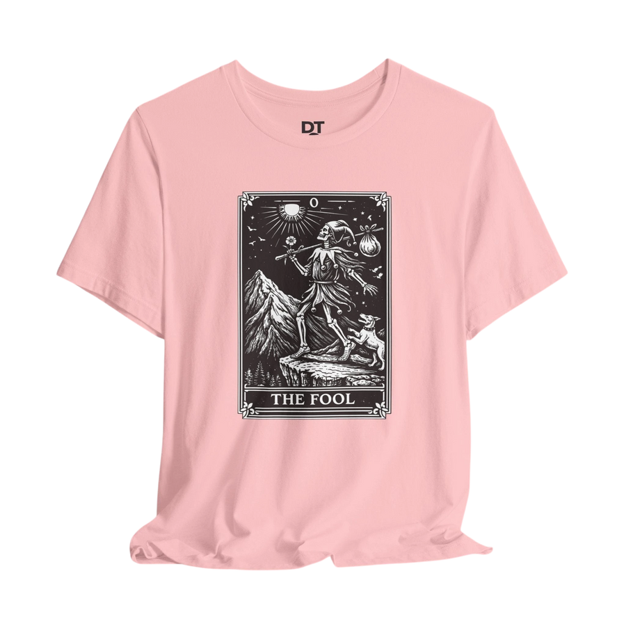 DailyThreadCo. pink cotton t-shirt with 'The Fool' tarot card graphic in black and white. Features a skeleton figure with a dog and mountain landscape.