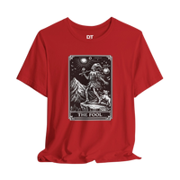 DailyThreadCo. red cotton t-shirt with 'The Fool' tarot card graphic print on front. Features skeleton figure, mountains, dog, and celestial details.
