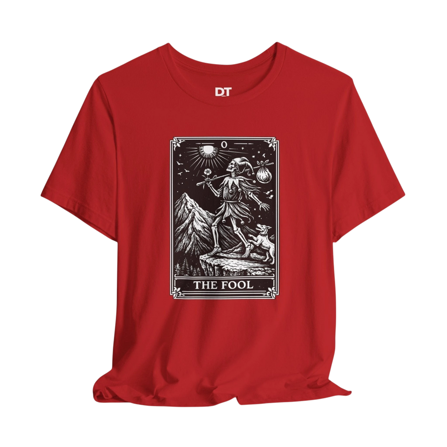 DailyThreadCo. red cotton t-shirt with 'The Fool' tarot card graphic print on front. Features skeleton figure, mountains, dog, and celestial details.