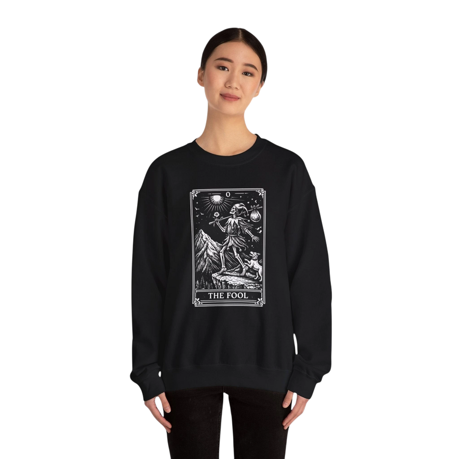 DailyThreadCo black crewneck sweatshirt with a vintage "The Fool" tarot card graphic, featuring a skeleton figure on a mountain cliff with a dog.