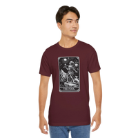 DailyThreadCo. maroon cotton t-shirt with 'The Fool' tarot card graphic print on the front. Features a skeleton figure on a mountain cliff with a dog.