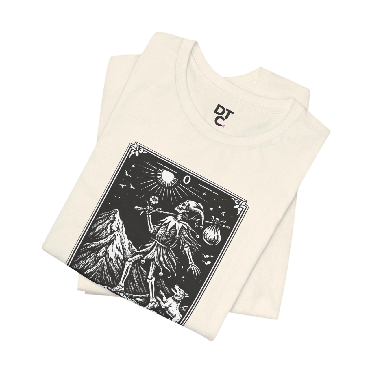 DailyThreadCo. cream cotton t-shirt with 'The Fool' tarot card graphic print in black and white, featuring a skeleton figure, mountain, sun, and dog.