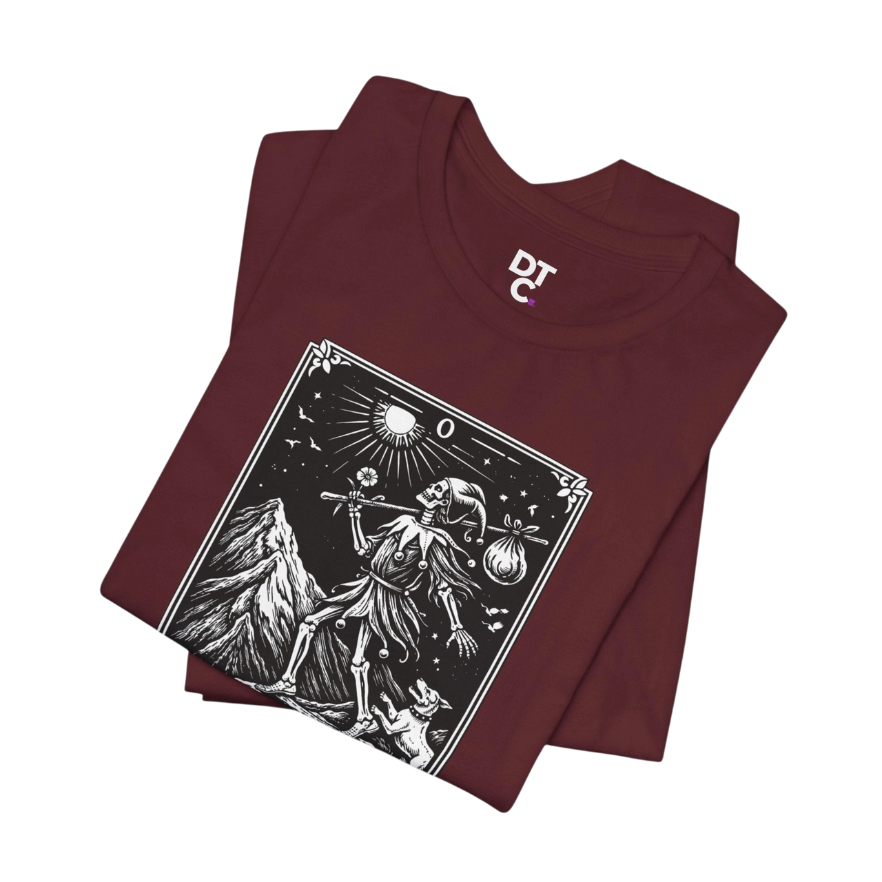 DailyThreadCo. maroon 100% cotton t-shirt with 'The Fool' tarot card graphic print. Features skeleton figure, mountain, sun, and dog.