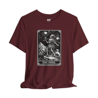 DailyThreadCo. maroon cotton t-shirt with 'The Fool' tarot card graphic print on front. Features skeleton figure, dog, mountains, and celestial symbols.