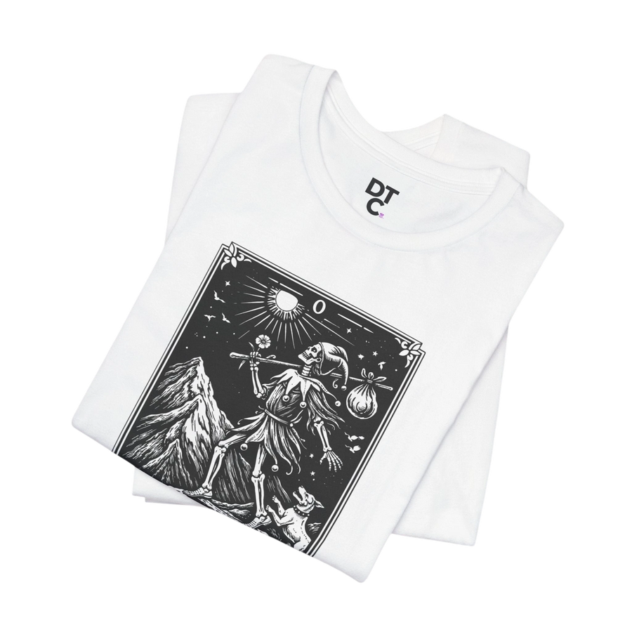 DailyThreadCo. white 100% cotton t-shirt with 'The Fool' tarot card graphic in black and white, featuring a skeleton figure, mountain, and celestial elements.